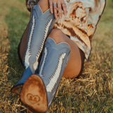 Person wearing blue cowboy boots with white patterns sitting on grass