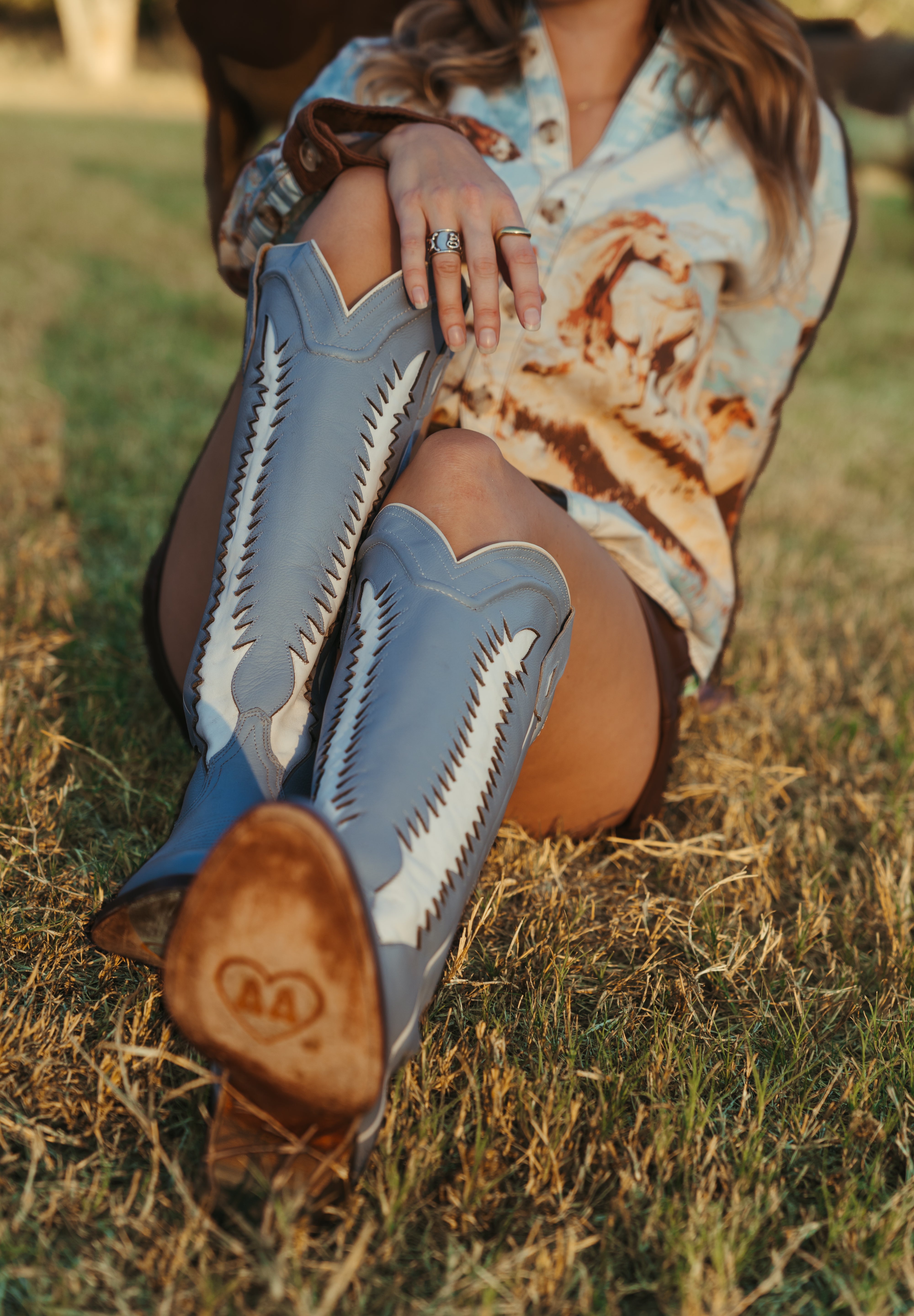 Person wearing blue cowboy boots with white patterns sitting on grass