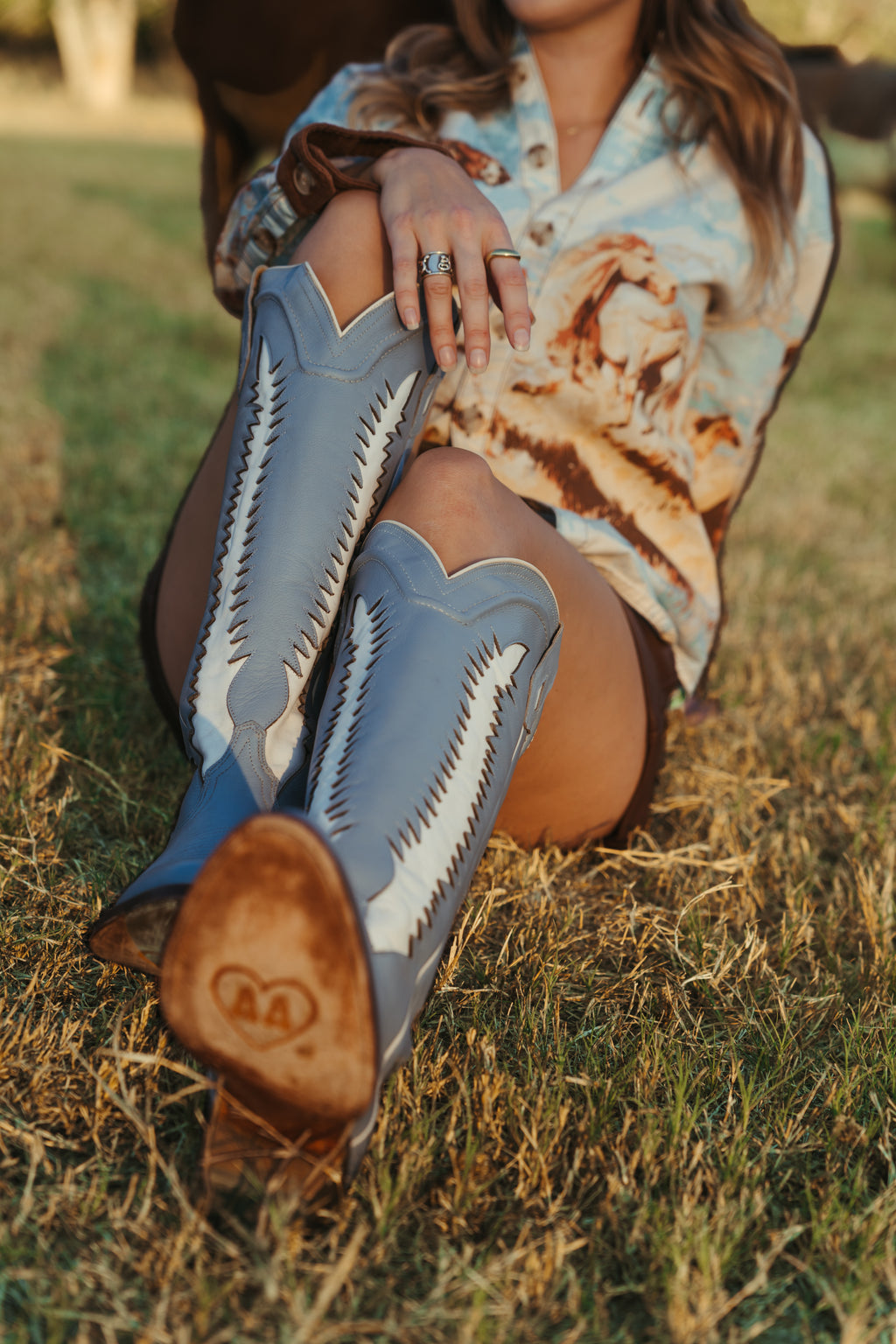 Person wearing blue cowboy boots with white patterns sitting on grass