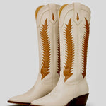 Pair of cream-colored cowboy boots with brown decorative patterns on a light gray background