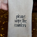 tan waffle weave dish towel with black Please Wipe the Counters embroidery on cowhide